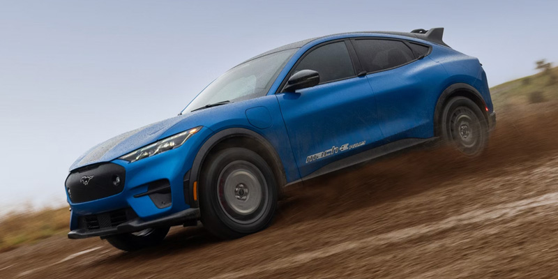 Blue Ford Mustang Mach-E Rally driving along a dirt path.