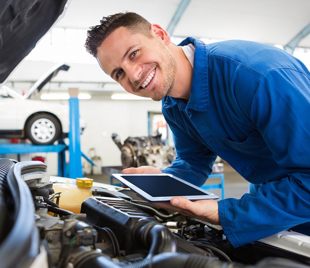 Person using a tablet computer while inspecting an open car engine